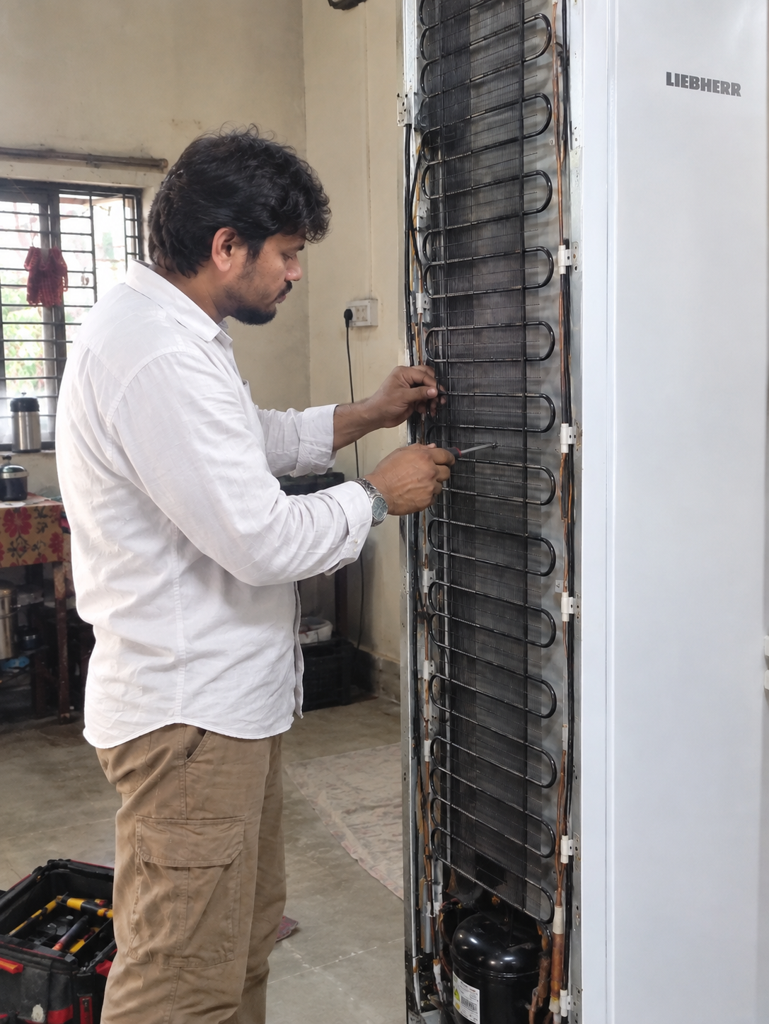 KLIMTECH technician repairing a refrigerator's cooling coils at a customer's home